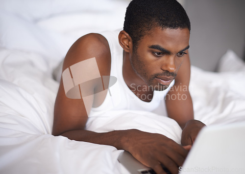 Image of Black man, bed and relax with laptop for research, social media or networking in duvet or sheets at home. African male person or freelancer typing on computer and lying in bedroom for online search