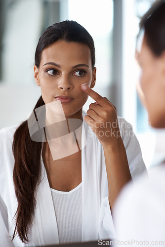 Image of Woman, mirror and beauty cream, skincare or cosmetics for facial routine and dermatology wellness. Young model or person applying moisturizer and product for eye care, sunscreen and makeup at home