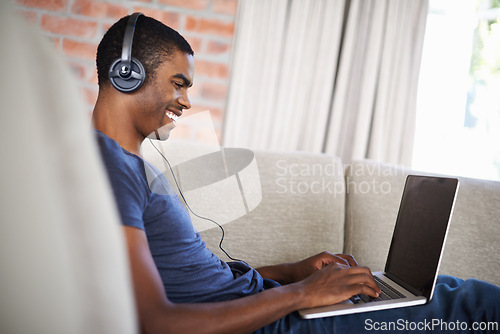 Image of Man, online and music with laptop on sofa for movie streaming, podcast and internet games with listening. Happy, black person and technology with headphones for relax, studying and learning in lounge