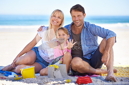 Image of Parents, girl and sandcastle in portrait at beach, blanket and excited with hug for holiday in summer. Father, mother and daughter with picnic by ocean for vacation in nature with love in sunshine