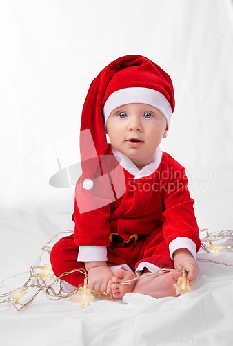 Image of Baby, portrait and cute with santa costume for first Christmas holiday, star lights and white background. Boy toddler, xmas and outfit for festive season or celebration, innocent and adorable in hat.