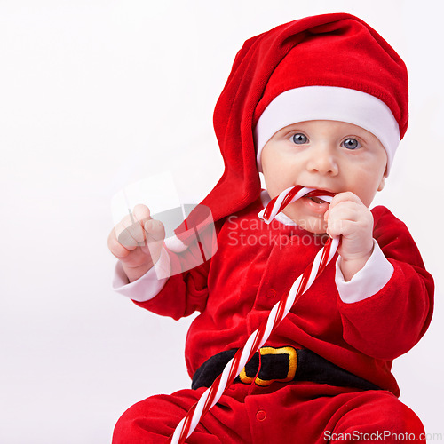 Image of Baby, portrait and studio with santa costume for first Christmas holiday, candy cane and white background. Boy toddler, xmas and outfit for festive season or celebration, innocent and adorable in hat