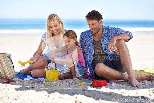 Image of Mom, dad and girl with sandcastle by sea on vacation with care, learning or building on holiday in summer. Father, mother and daughter with sand in plastic bucket for game, blanket and happy at beach