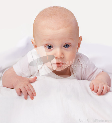 Image of Baby, blue eyes and shock with laying on bed for curiosity, surprise and reaction in bedroom at house. Adorable, child and cute infant with vest in home to observe, relax wonder for knowledge