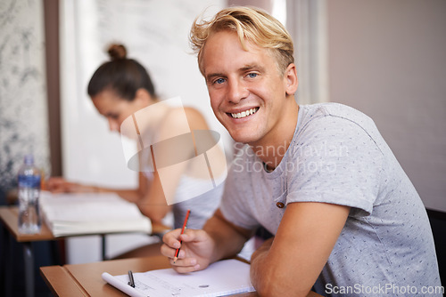 Image of Happy man, portrait and student with book in classroom for studying, reading or writing summary at university. Male person or academic writer with smile for assignment, test or exam on desk at campus