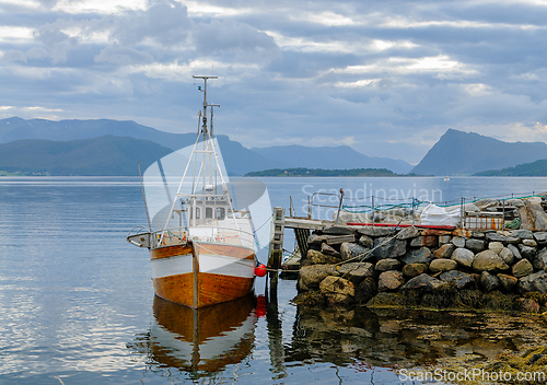 Image of Fishing boat moored at a rustic stone pier in serene coastal wat