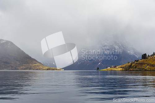 Image of Misty fjord surrounded by snow-capped mountains during a calm wi