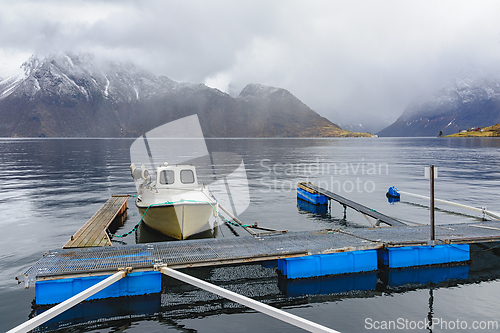 Image of Small boat moored at a wooden dock on a calm mountain fjord duri