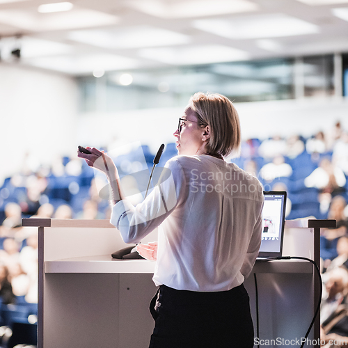 Image of Female speaker giving a talk on corporate business conference. Unrecognizable people in audience at conference hall. Business and Entrepreneurship event.