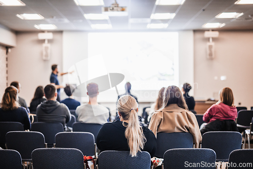 Image of Speaker giving a talk in conference hall at business event. Rear view of unrecognizable people in audience at the conference hall. Business and entrepreneurship concept.