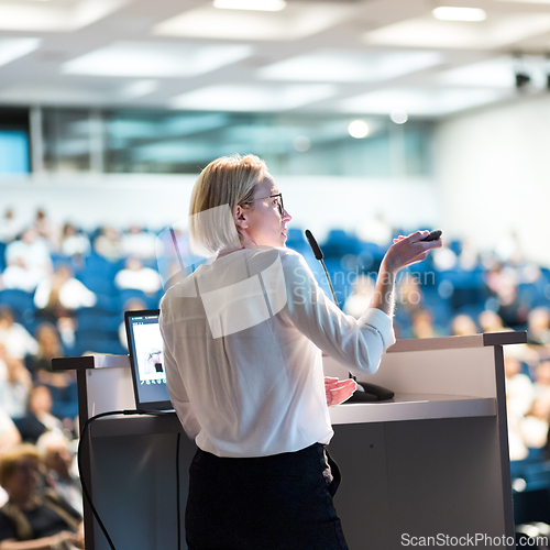 Image of Female speaker giving a talk on corporate business conference. Unrecognizable people in audience at conference hall. Business and Entrepreneurship event.