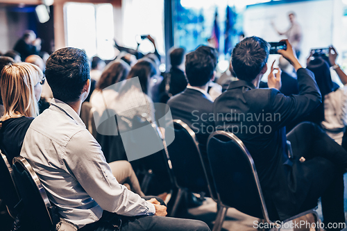 Image of Speaker giving a talk in conference hall at business event. Rear view of unrecognizable people in audience at the conference hall. Business and entrepreneurship concept.