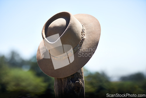 Image of Cowboy hat, outdoor and wood post for protection from sun with fashion at ranch, countryside and nature. Vintage cap, headwear and shade from sunshine with farming, agriculture and summer in Texas