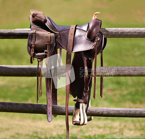 Image of Saddle, horse and farm on ranch fence, riding and equestrian sports in country side. Western, cowboys and field in Texas, stirrup and leather seat or equipment for outdoors exercise in paddock