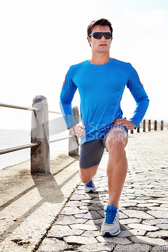 Image of Man, ocean and stretching for fitness with workout to jog, health and wellness with body care in Chicago. Male person, sportswear and active as runner with sunglasses for exercise, beach or committed