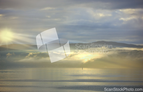 Image of Sea, sunset and cloud on mountains in morning, reflection and island with landscape in nature. Blue sky, clouds or sunlight on water on beach, calm or sunrays on sustainable environment or seascape