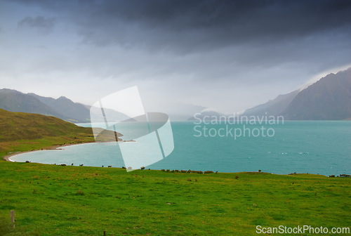 Image of Lake, mountains and nature with view of green scenery on foggy or misty morning outdoor in spring. Earth, sky and water with grass on ground in natural ecosystem or environment of New Zealand