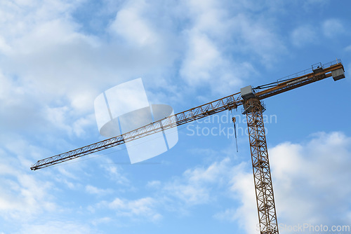Image of Crane, outdoor and clouds or blue sky background for building with heavy machinery or construction material. Hoist in city, urban or industrial development with low angle, tools or overhead equipment