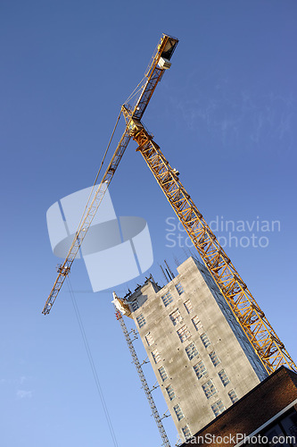 Image of Crane, construction and site on blue sky background for building with heavy machinery in architecture or engineering. Hoist in city, urban or industrial development in low angle of overhead equipment