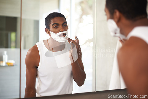 Image of Black man, mirror and shaving cream on face in bathroom for grooming, skincare or morning routine. Reflection, beard and person apply foam for cleaning, health and hair removal for hygiene in home