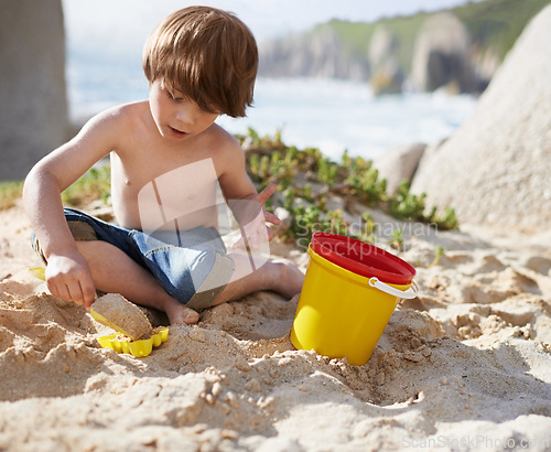 Image of Sand castle, beach and child with bucket and toys on summer holiday, vacation and relax by ocean. Childhood, building or digging and young boy playing for adventure, fun and weekend by seaside