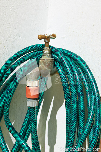 Image of Tap, pipe and garden hose with attachment for water, pressure or environmental care at home. Closeup of faucet with plastic hosepipe rolled up on wall for liquid supply, service or outdoor gardening