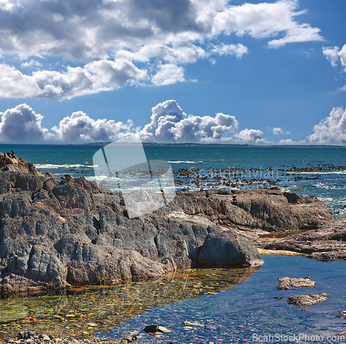 Image of Rocks, ocean and landscape with nature, blue sky and clouds with coastline and outdoor travel destination. Surf, Earth and water with seascape, natural background and beach location in Cape Town