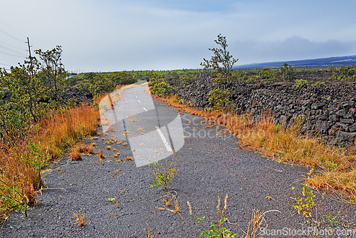 Image of Road, landscape and volcano street in nature with lava rocks, plants and grass for travel, adventure and roadtrip. Dead end, deserted path and location in Hawaii with blue sky, roadway or environment