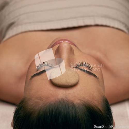 Image of Massage, spa and stone on head of woman on table to relax with stress relief or luxury treatment. Calm, wellness and zen with young beauty customer on table for balance, inner peace or mindfulness