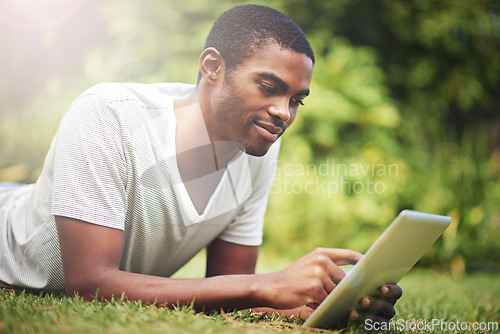 Image of Relax, happy and tablet with black man on grass of garden for research or information in summer. Technology, internet and young person reading online ebook on green field outdoor in backyard