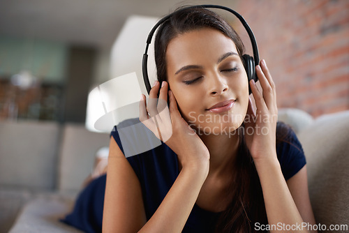 Image of Face, music and relax with woman on sofa in living room of home to smile for free time break. Headphones, peace and radio with young person lying on couch in apartment for weekend chilling or rest