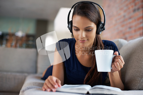 Image of Book, coffee and music with woman on sofa in living room of home, reading to relax at weekend. Storytelling, headphones and drinking tea with young person in apartment for hobby, leisure or time off