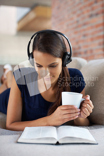 Image of Music, book and woman relax with coffee in home on holiday or vacation and headphones streaming audio. Girl, reading and listening to sound on sofa in apartment on weekend with green tea or drink