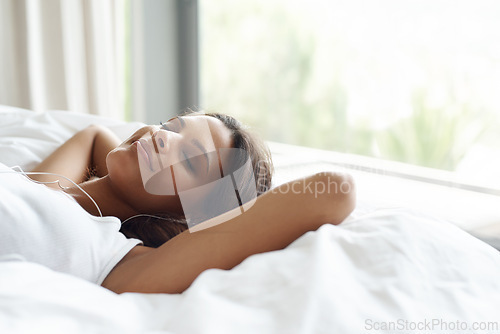 Image of Woman, sleep and bed with earphones for music, listening to relax in morning at home for peace or rest. Female person, comfortable and lay with smile and calm in house for wellness with podcast.