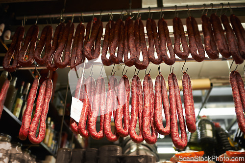 Image of Hooks, butchery and dry sausage in shop for traditional food, groceries or products in Germany. Supermarket, meat and fermented or smoked salami hanging in row for production in grocery store.