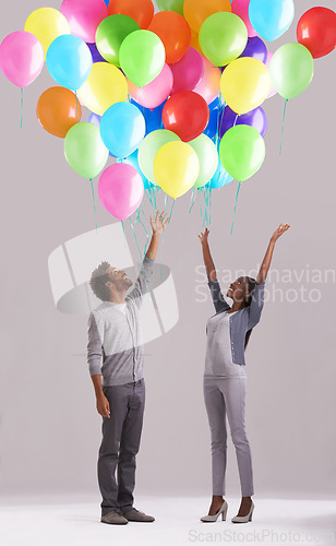 Image of Happy couple, party and celebration with balloons for event, birthday or romance on a gray studio background. Excited man and woman with colorful blowups of helium for date, giveaway or anniversary