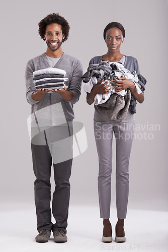 Image of People, studio and pile of washing in hand for wash, laundry day and couple cleaning together. Happy, man and neat clothes folded with woman, messy and unhappy for dirty wardrobe on gray background