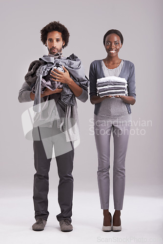 Image of Portrait, studio and people with pile of clothes in hand for laundry day, wash or cleaning together. Woman, smile and washing folded with messy, man and annoyed for dirty wardrobe on gray background