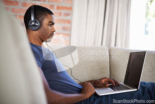 Image of Man, internet and music with laptop on sofa for movie streaming, podcast and online games with listening. Young, black person and technology with headphones for relax, studying and learning in lounge