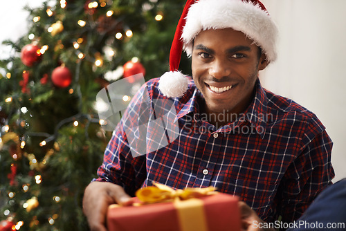 Image of African, man and gift for christmas, portrait and holiday with smile for vacation. Person, happiness and celebration for present, house and tree with decorations, giving or festivity at home with hat