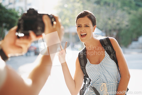 Image of Tourist, woman and photography with peace sign for travel, sightseeing or memories on holiday or vacation in street. People, person or funny face in city for explore, tourism or journey in urban town