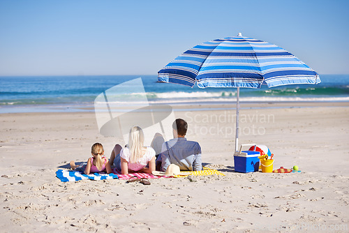 Image of Family, relax and lying on beach with umbrella for summer holiday, vacation or outdoor weekend together in nature. Rear view of father, mother and daughter chilling on towel or sand by ocean coast