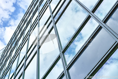 Image of Low angle, construction and building with glass windows in city for business, office and commercial property with sky. Closeup, architecture and real estate for hotel, accommodation and skyscraper