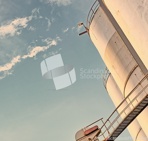 Image of Closeup, silo and tank at plant for agriculture, bulk storage and product safety with sky, clouds and outdoor. Container, agricultural structure and oil refinery tower with low angle for distillery