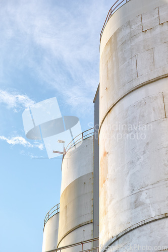 Image of Closeup, silo and tank at plant for agriculture, bulk storage and product safety with sky, clouds and outdoor. Container, agricultural structure and oil refinery tower with distillery for business