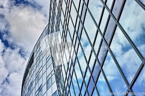 Image of Low angle, architecture and building with glass windows in city for business, office and commercial property with sky. Clouds, construction and real estate for hotel, accommodation and skyscraper