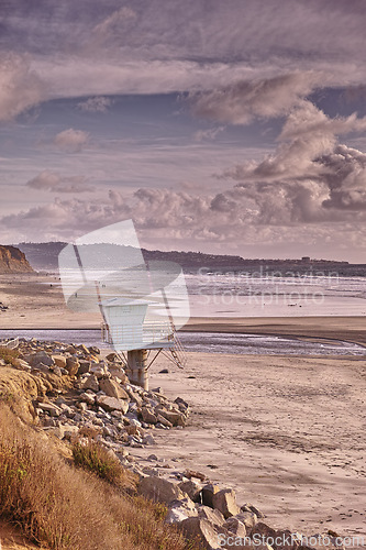 Image of Beach, landscape and lifeguard tower in summer, morning and travel to island in Norway for vacation or holiday. Ocean, waves and calm water at coast with clouds in sky and mountain on horizon