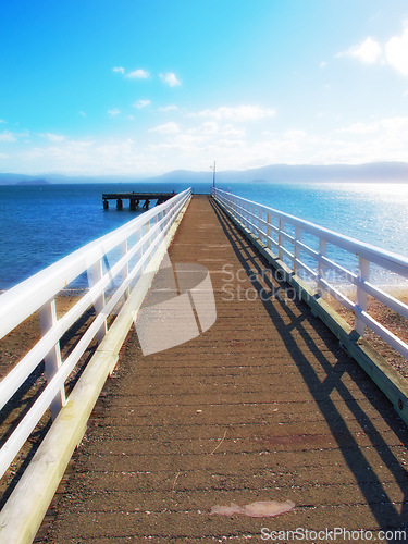 Image of Mountain, ocean and wooden pier on island with blue sky, tropical landscape and travel in Indonesia. Beach, vacation and relax on wood bridge, jetty or dock with sea water, clouds and summer in Bali