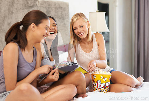 Image of Friends, popcorn and reading magazine on bed with laughing, discussion and girls night in home with pyjamas. Women, snack and happiness with paper in house for bonding, conversation and excited