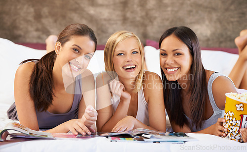 Image of Happy friends, portrait and girls reading magazine in bedroom, food and eating popcorn snack together at party. Smile, women and group with journal in home, face and laugh in bed to relax in house